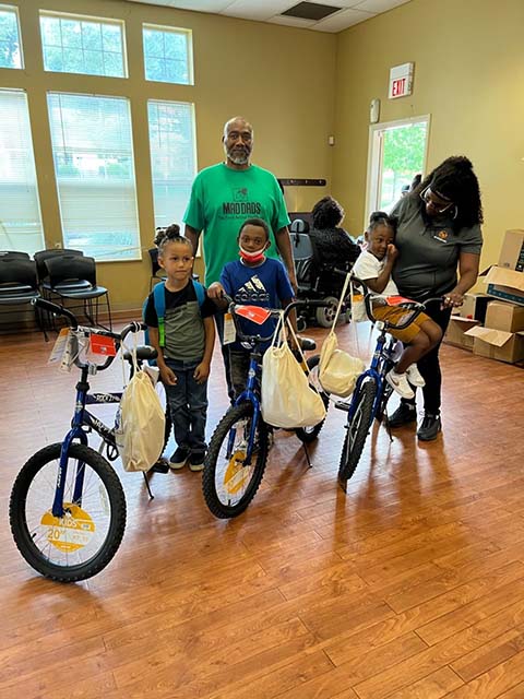 Children and a parent with new bicycles at a MAD DADS community giveaway